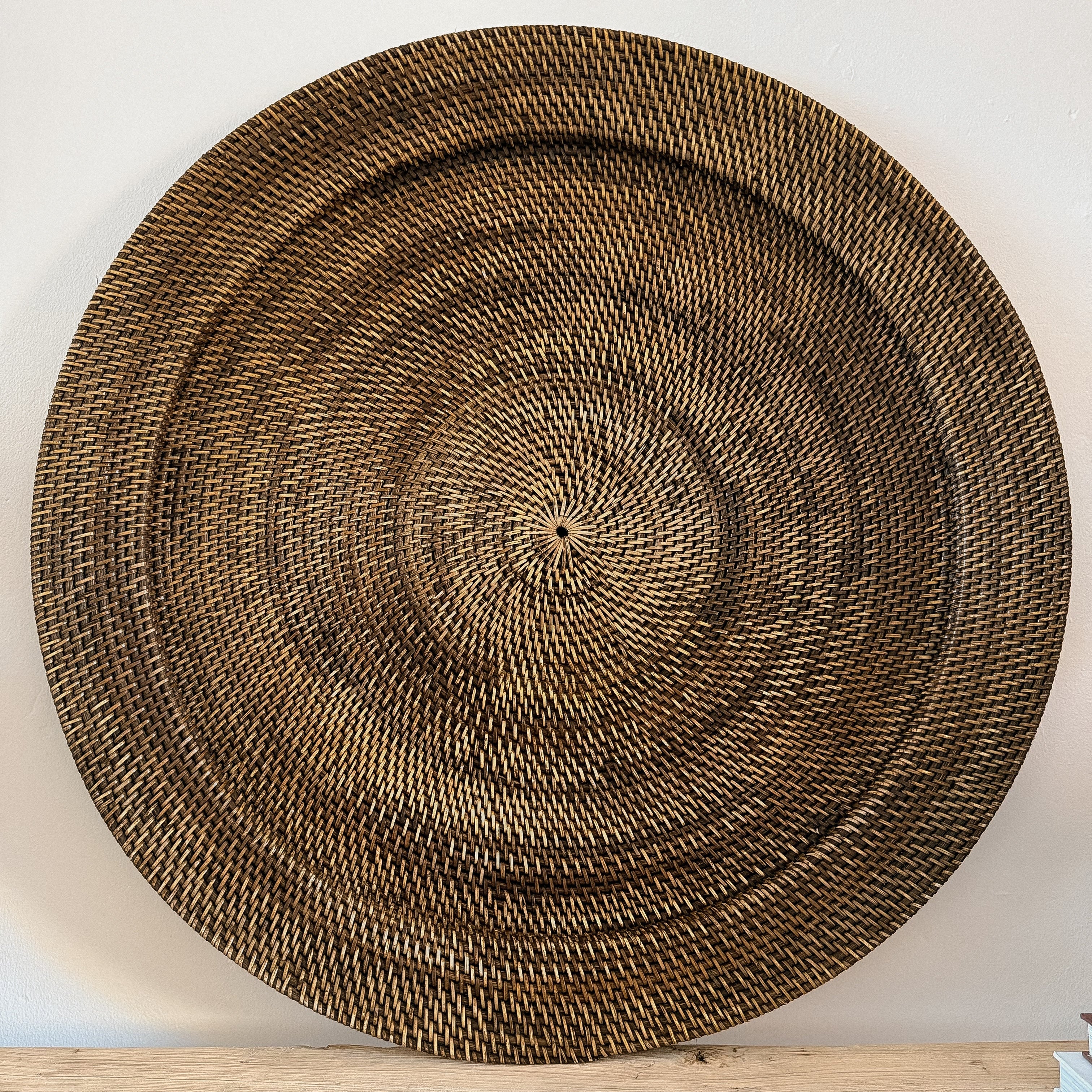 A large round rattan hand woven wall hanging finished in dark brown sat on a wooden table top