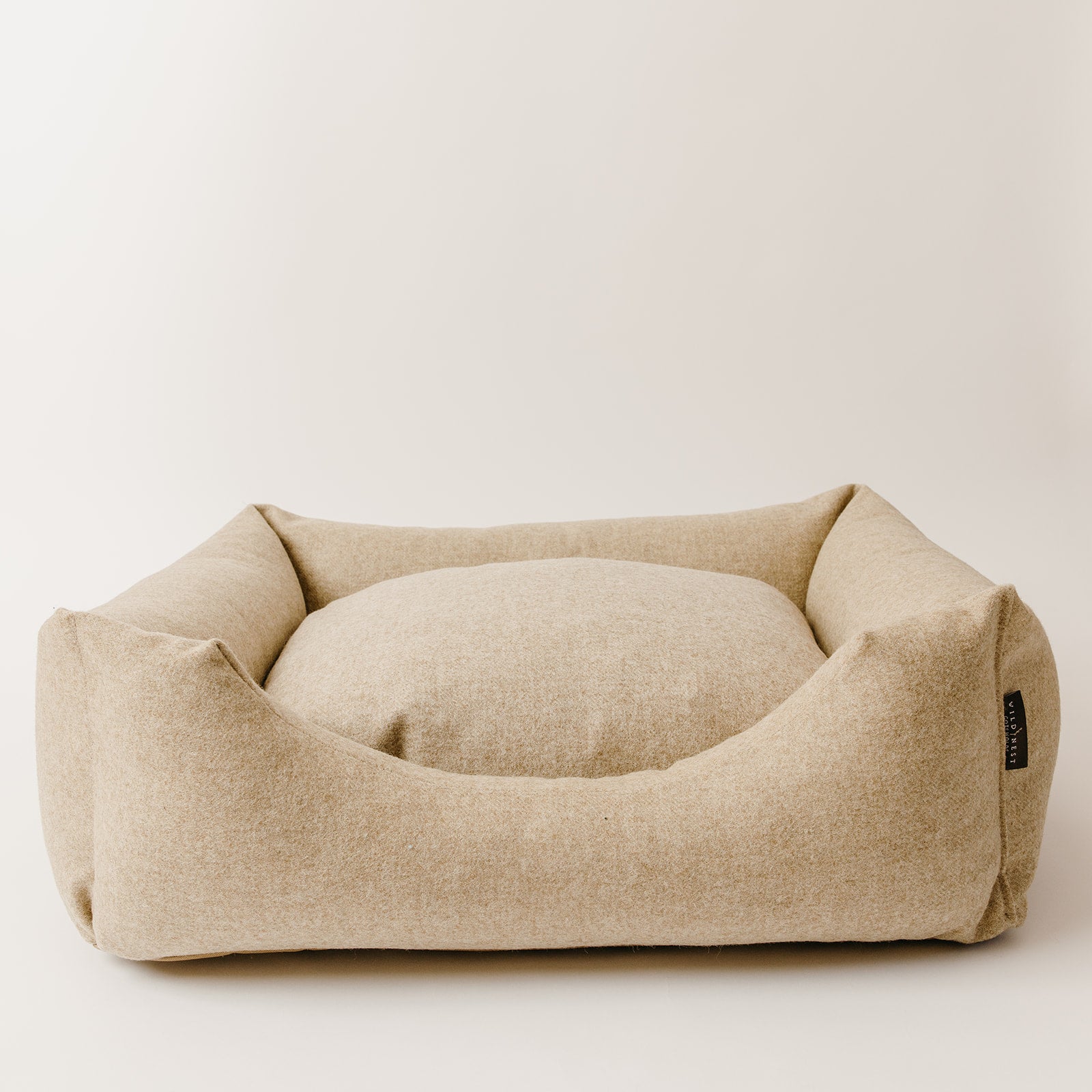 handmade luxury wool dog bed by Wild Nest Cotswolds, upholstered in natural oatmeal fabric on a plain white studio background