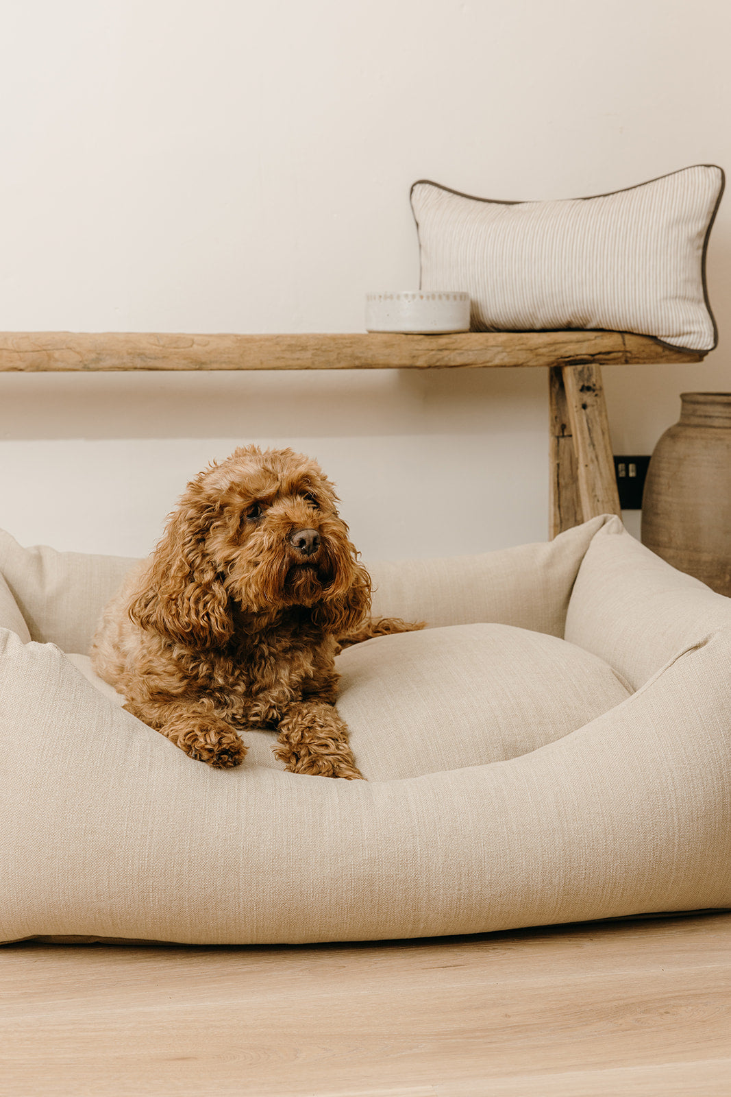 Cotton linen mix luxury dog bed in warm beige with a small dog relaxing inside, handcrafted in England and styled in a neutral Cotswold home.