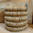 A chunky round woven basket made of water hyacinth with two loop handles, stacked on a light wood floor in an indoor setting.
