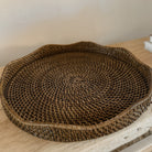 Handwoven scallop rattan tray in a dark brown finish on an elm console table against a beige wall.
