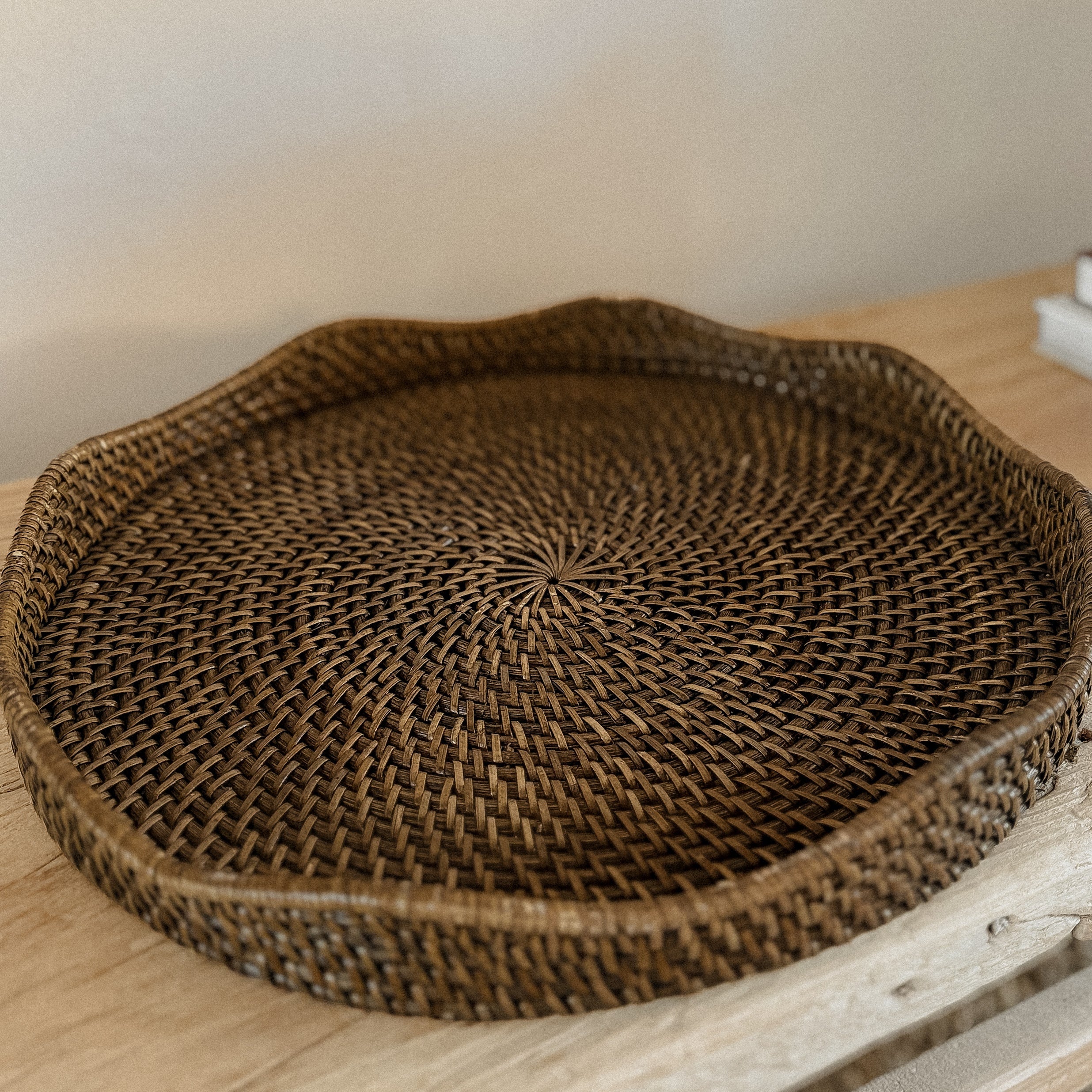 Handwoven scallop rattan tray in a dark brown finish on an elm console table against a beige wall.