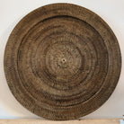A large round rattan hand woven wall hanging finished in dark brown sat on a wooden table top 