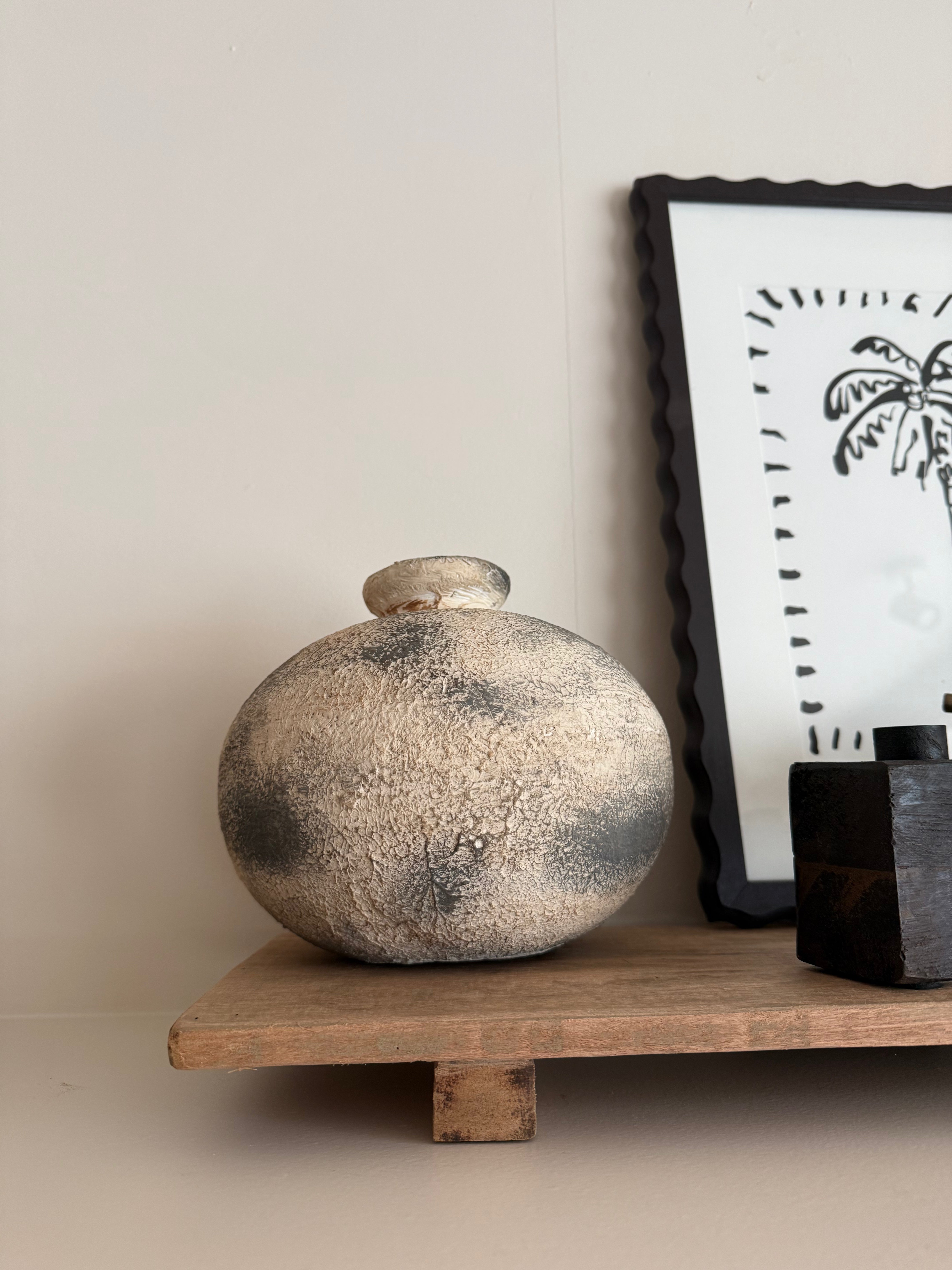 Decorative vase on a wooden shelf with a framed picture in the background