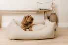 Cotton linen mix luxury dog bed in warm beige with a small dog relaxing inside, handcrafted in England and styled in a neutral Cotswold home.