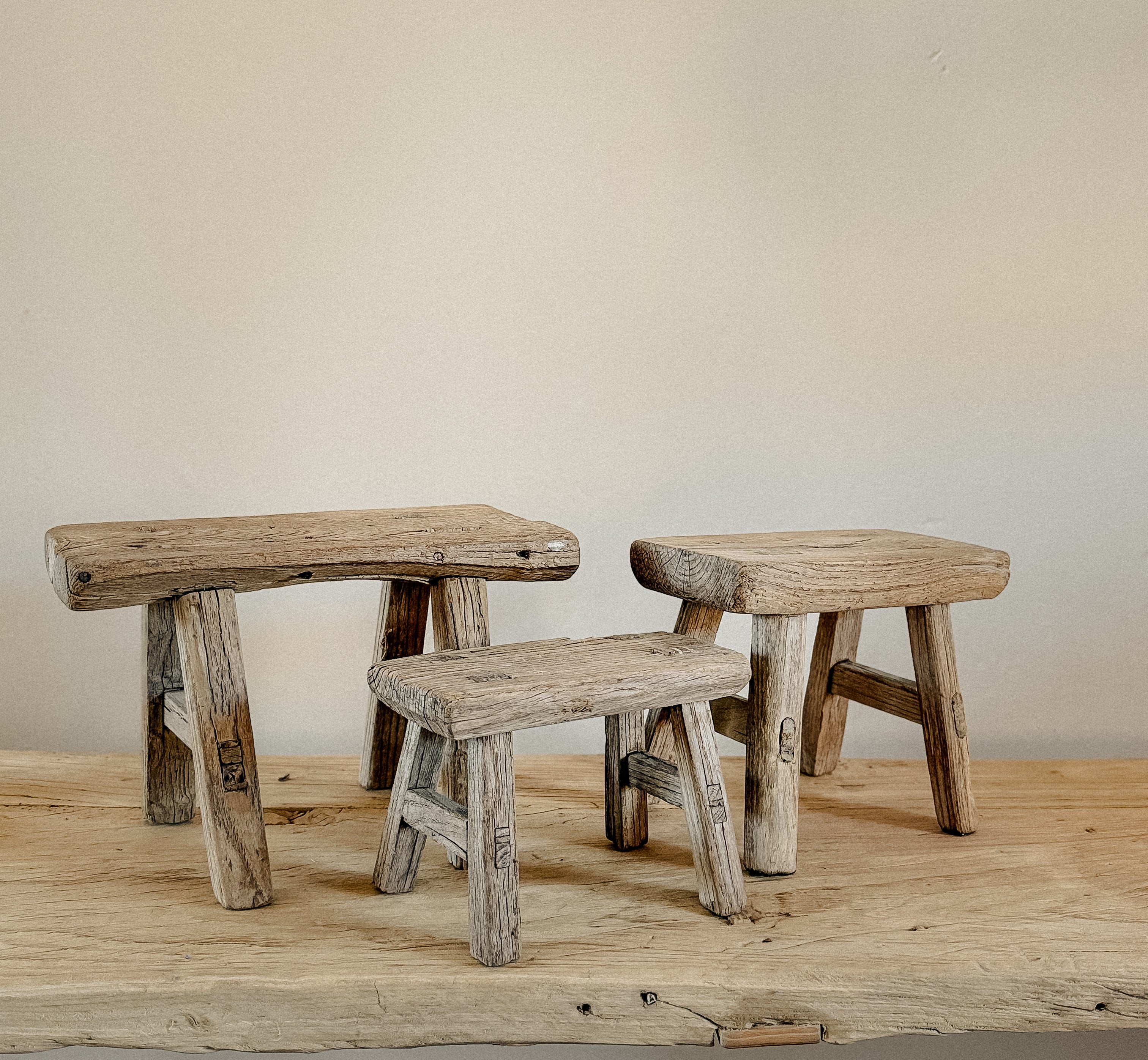 Three rustic elm wooden stools on a wooden floor with a plain wall background