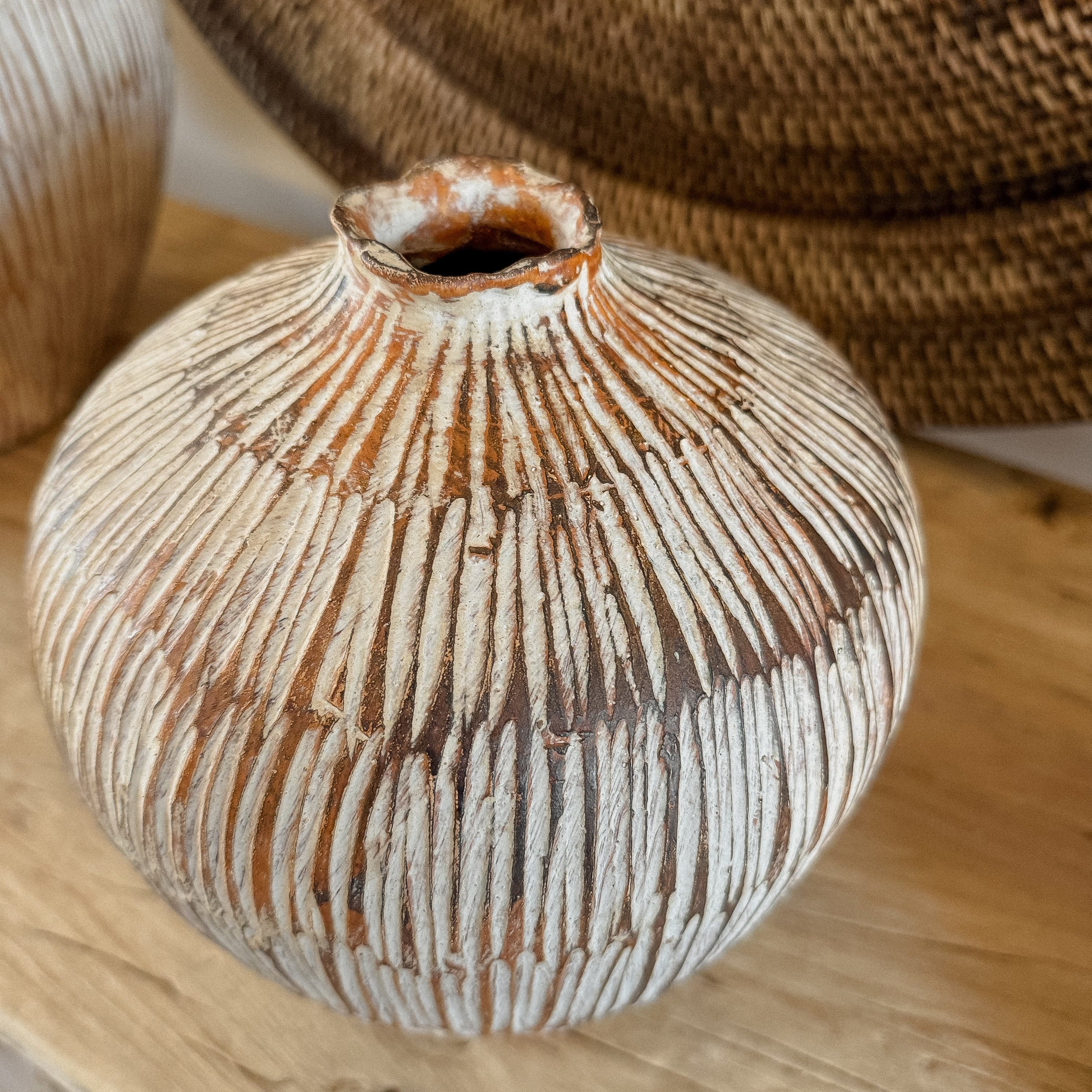 Close up image of the texture on a terracotta vase with unique hand carved design, sat on an elm console table top 