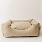 handmade luxury wool dog bed by Wild Nest Cotswolds, upholstered in natural oatmeal fabric on a plain white studio background