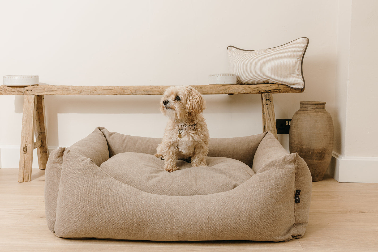 Dog sitting on a luxury linen cotton dog bed in a neutral home setting